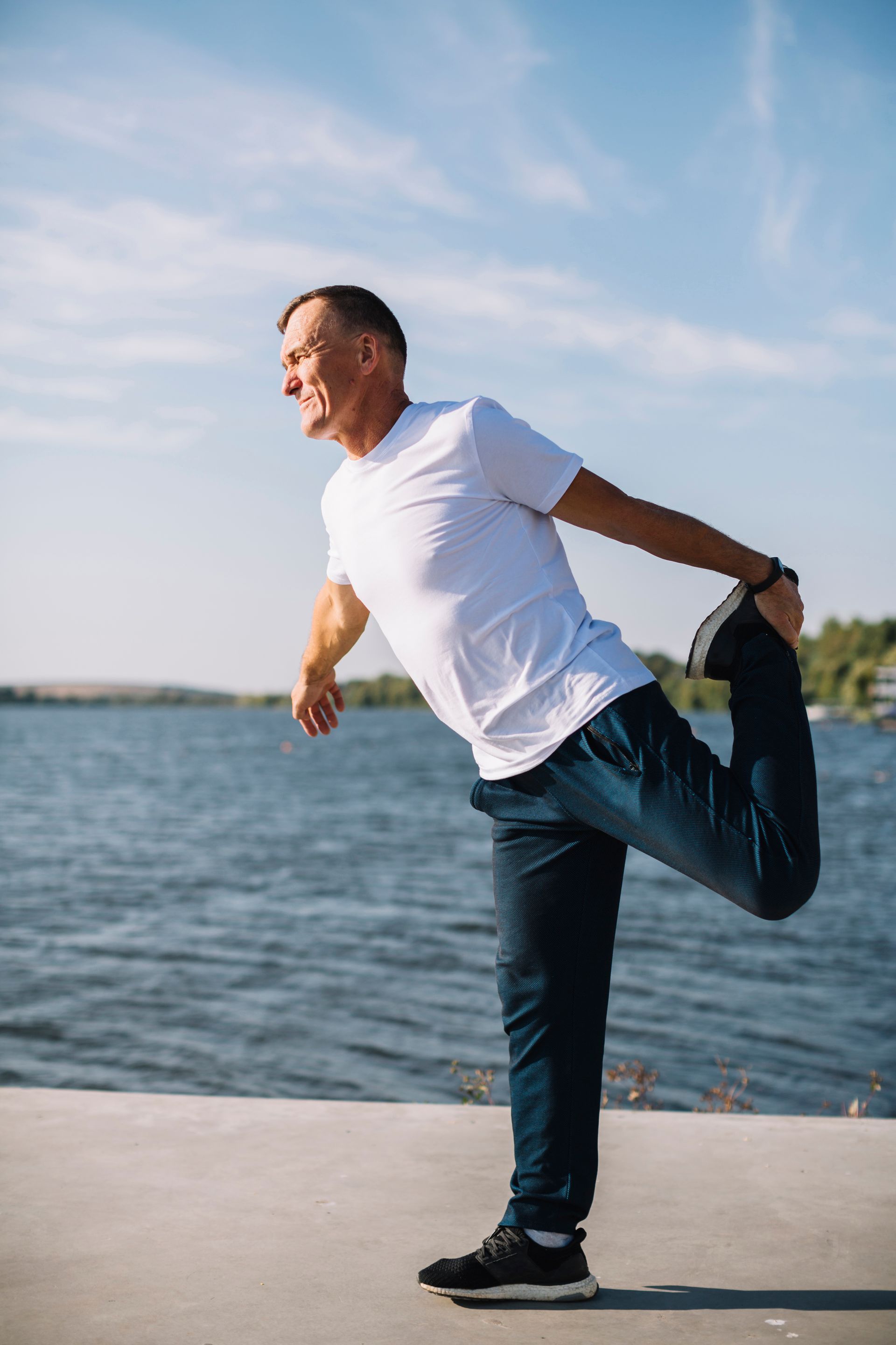 A man is stretching his leg in front of a body of water.
