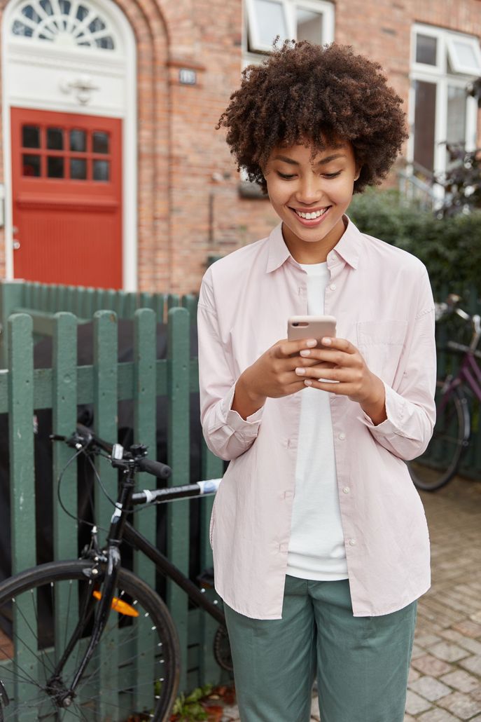 A woman is standing in front of a fence looking at her cell phone.