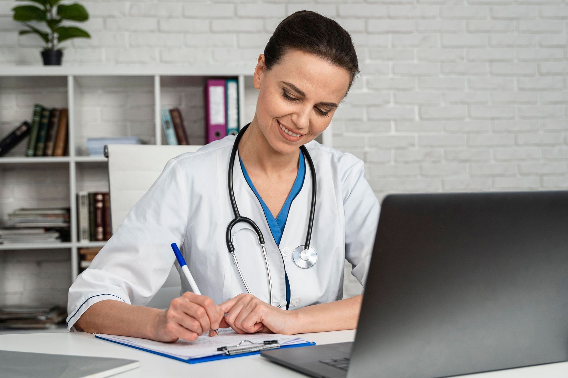A female doctor is sitting at a desk in front of a laptop computer.