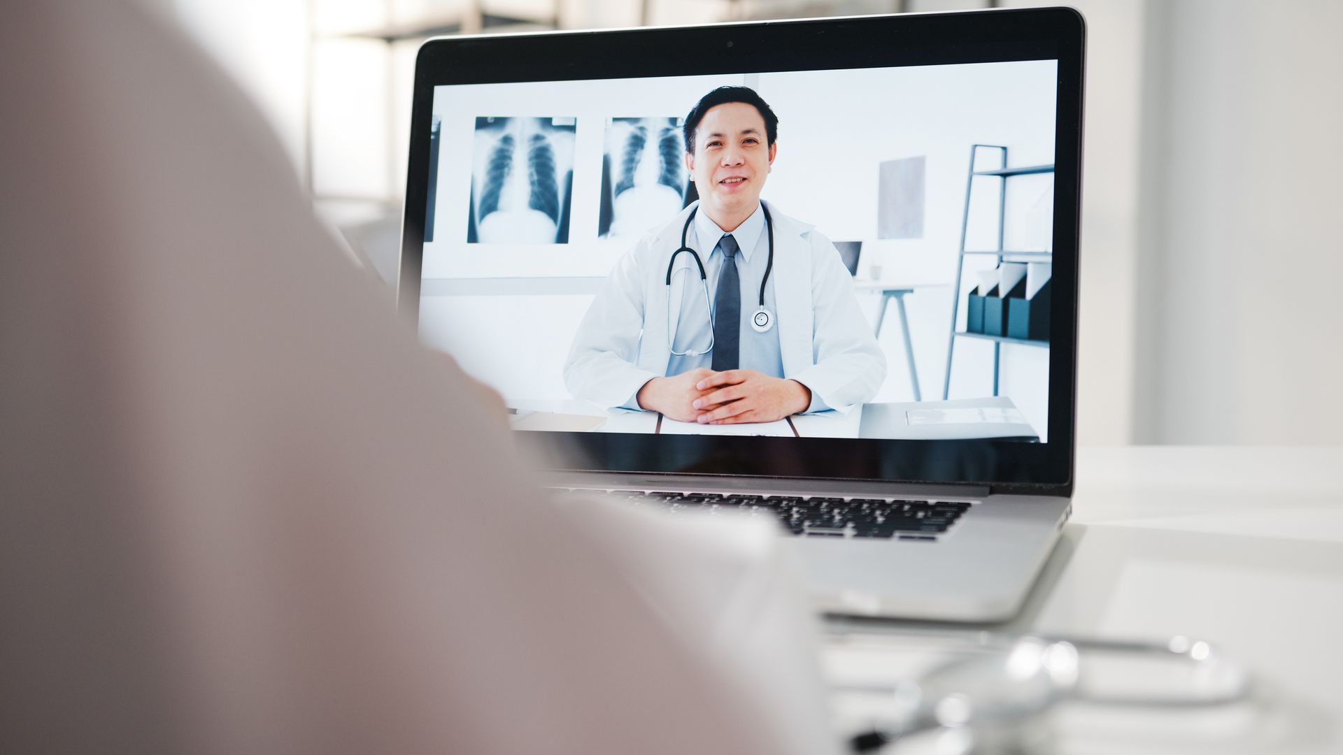 A doctor is having a video call with a patient on a laptop.