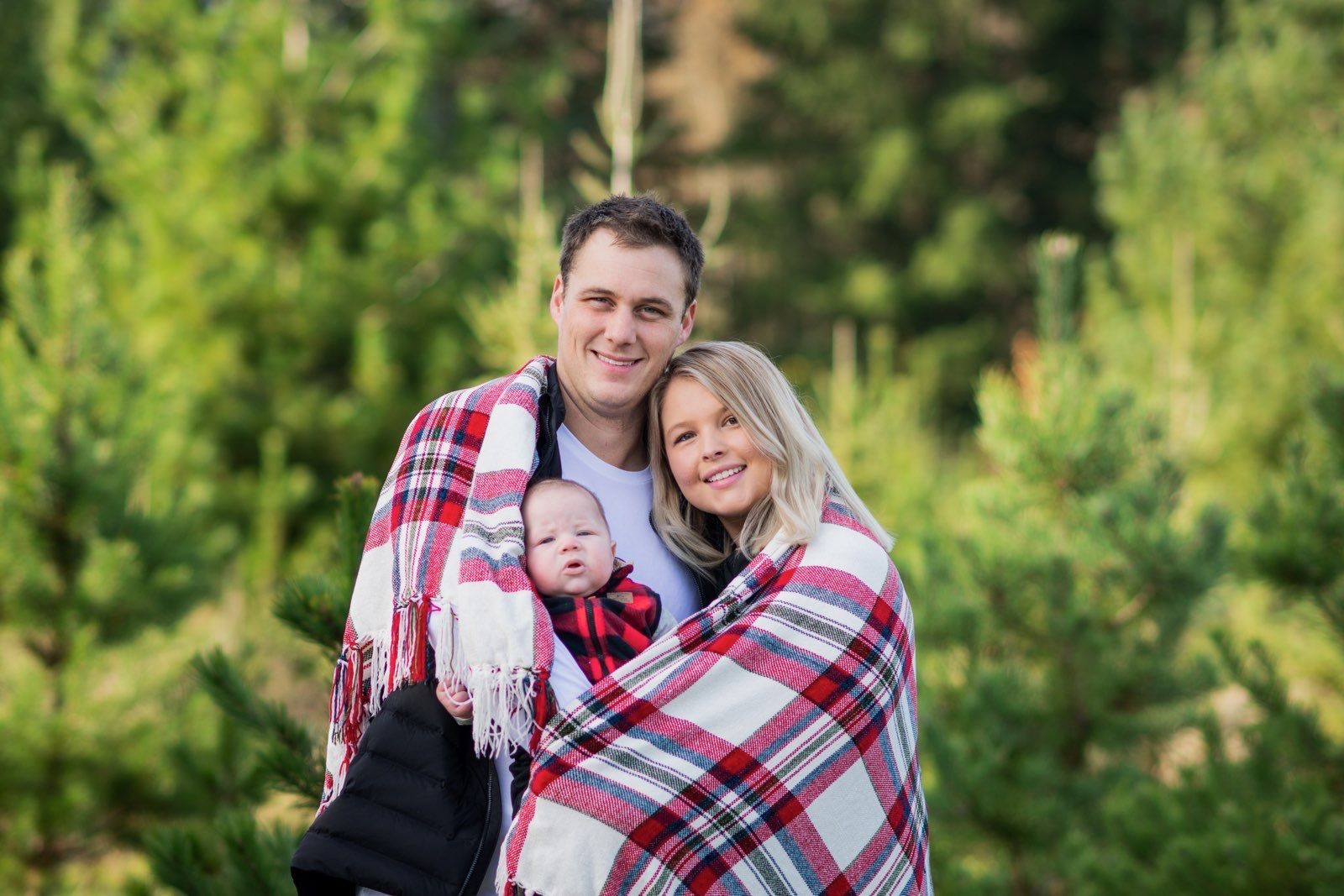 A man and woman are holding a baby wrapped in a plaid blanket from Washington Roofing Services near Arlington WA