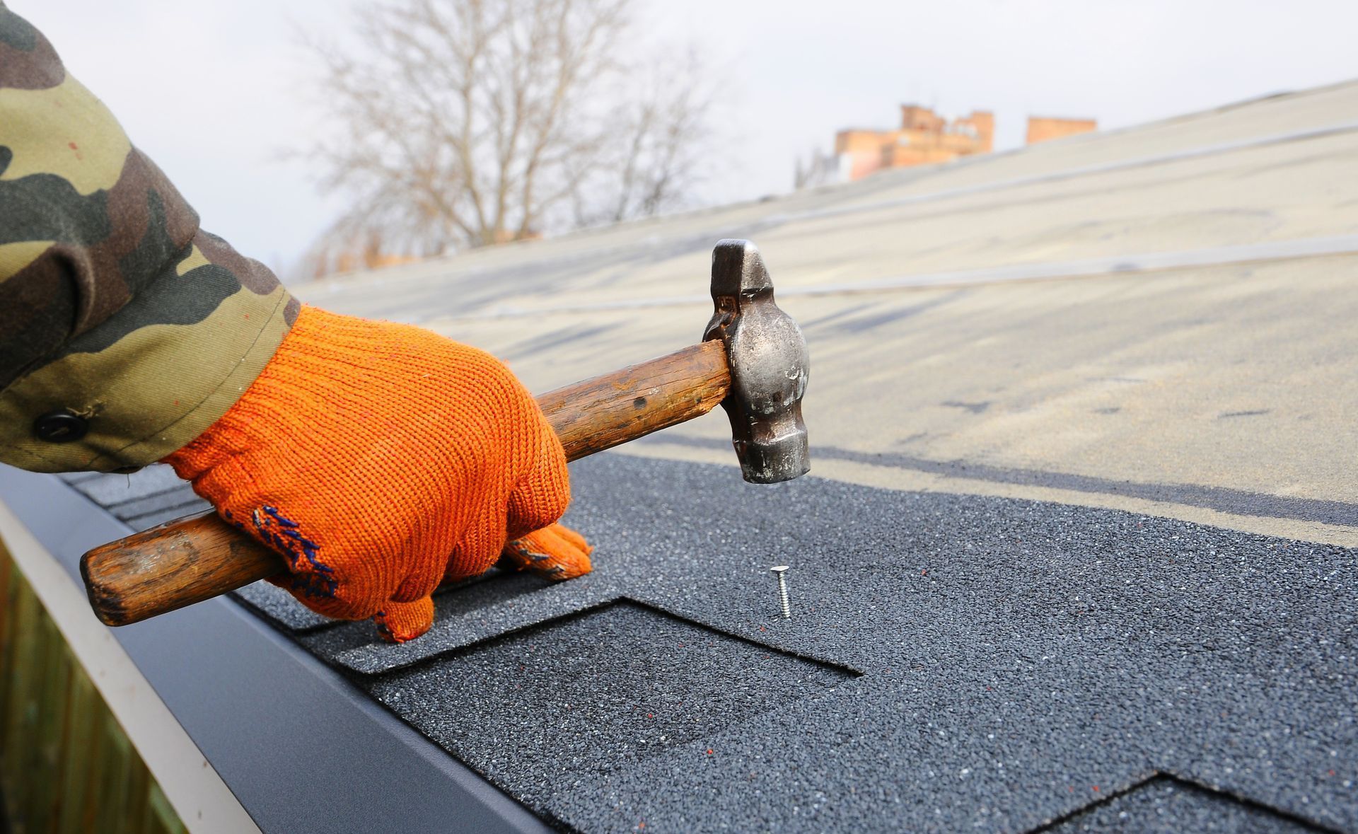 A person is hammering a nail into a roof with a hammer from Washington Roofing Services near Arlington WA