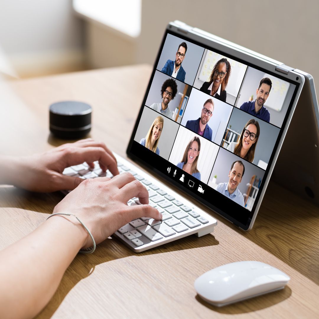 A person is typing on a laptop with a group of people on the screen.