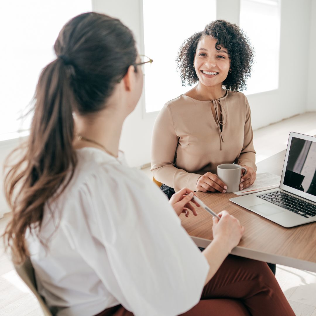 Two women are sitting at a table with a laptop and a cup of coffee