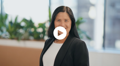 A woman in a black jacket and white shirt is standing in front of a window.