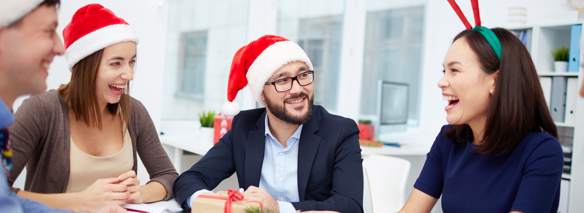 A group of people wearing santa hats are sitting around a table.