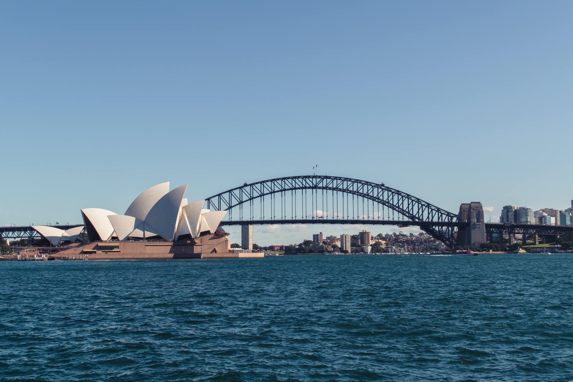 The sydney harbor bridge and the opera house are visible from the water.