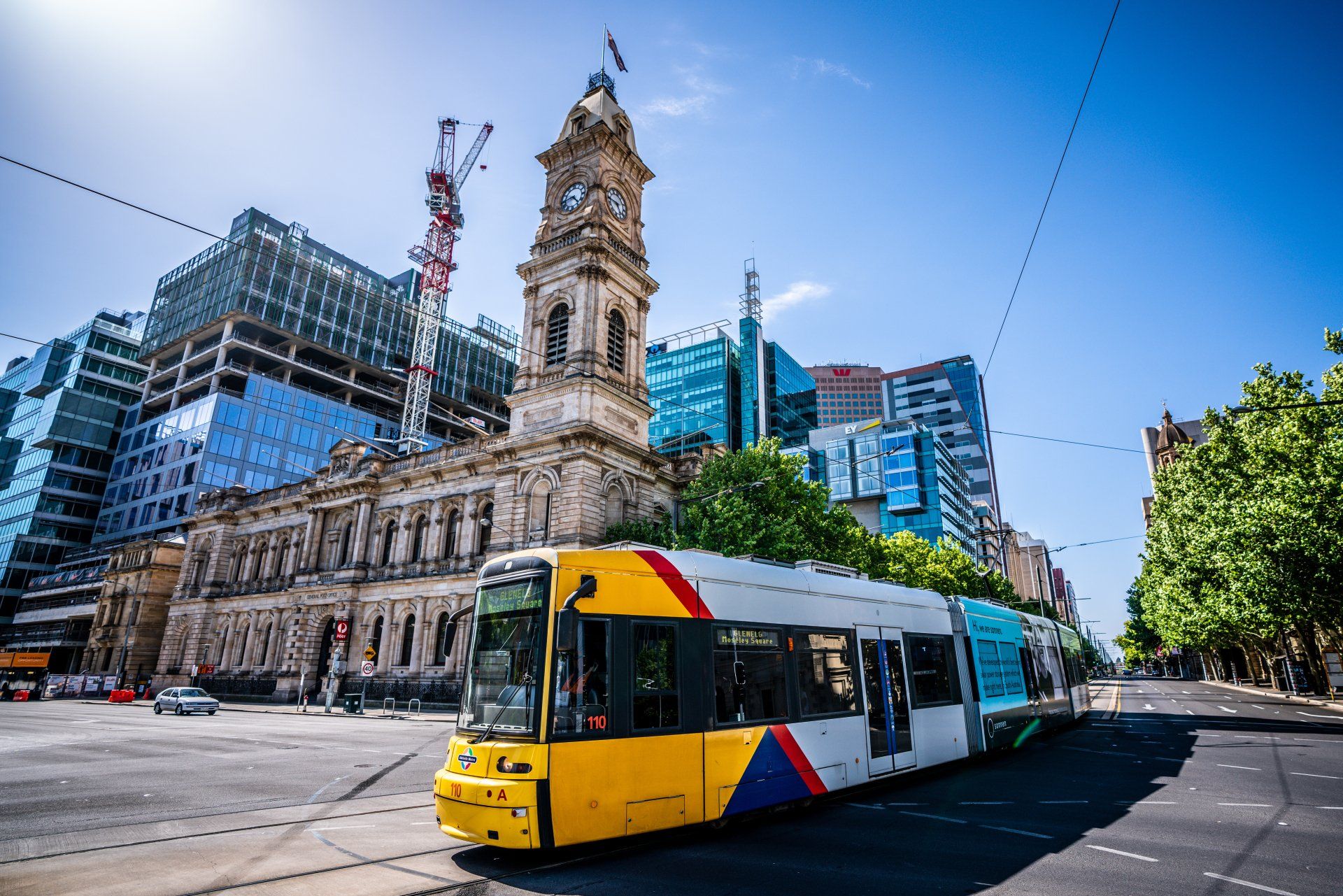 A yellow trolley is driving down a city street in front of a building with a clock tower.