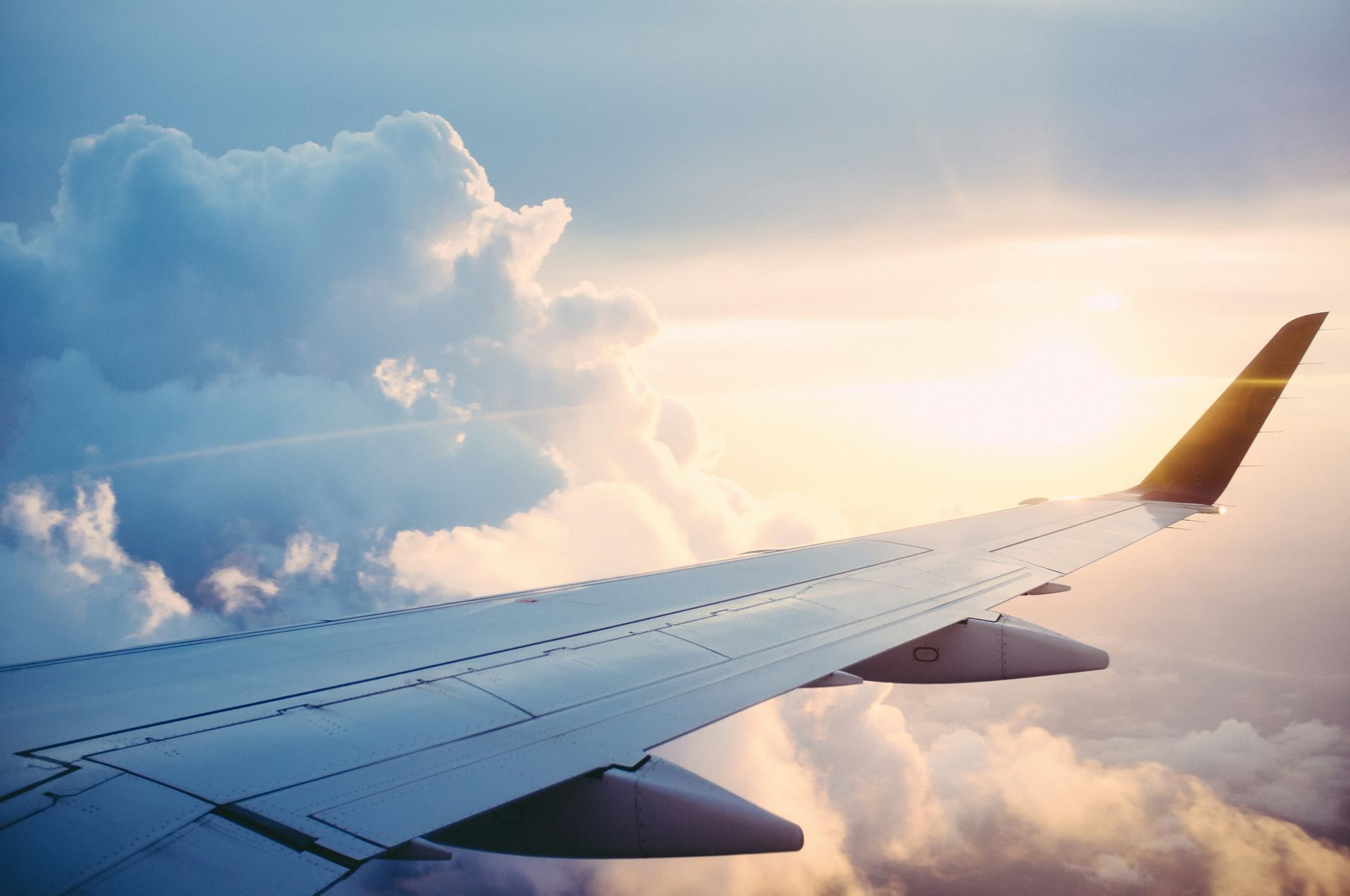 The wing of an airplane is flying through the clouds at sunset.