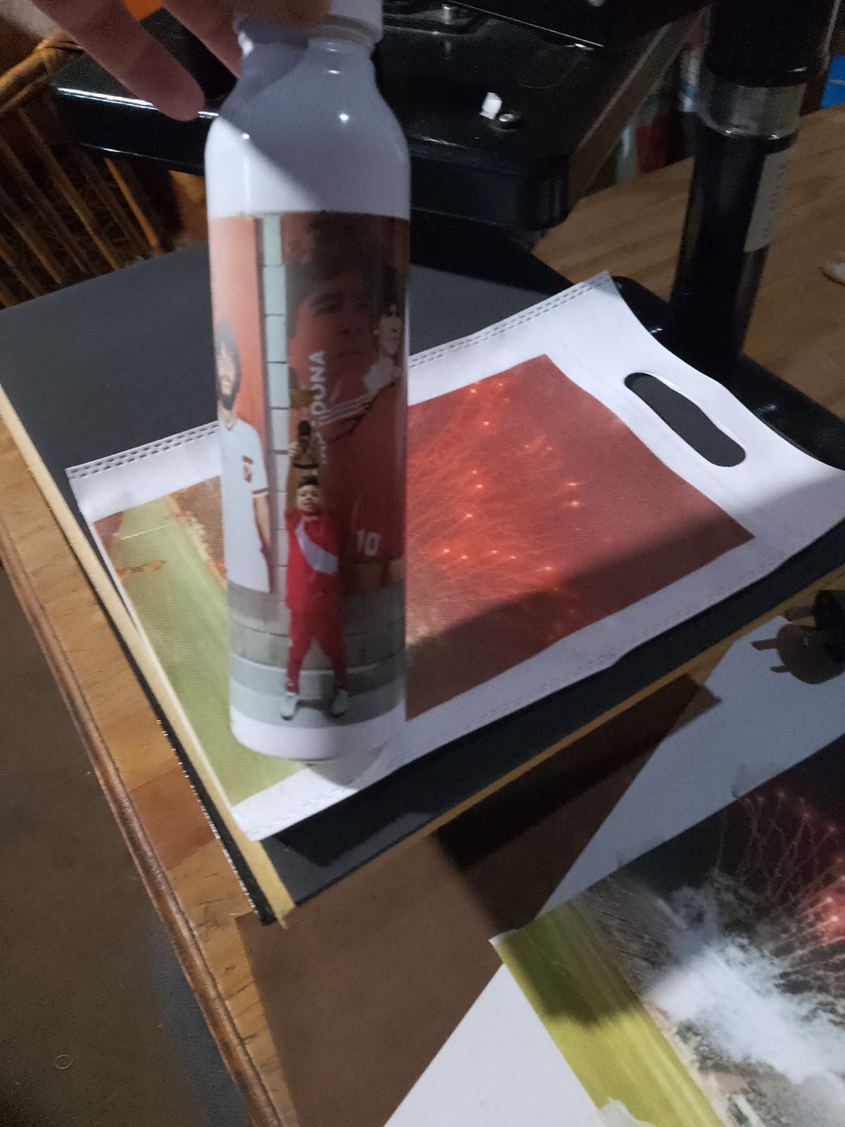 Botella de agua blanca con imagen impresa, sostenida sobre una superficie con imágenes impresas