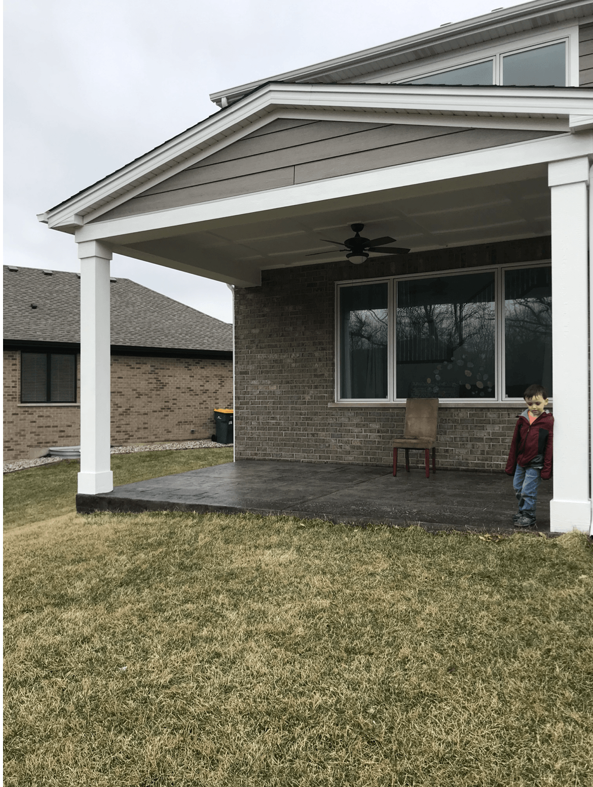 A boy is standing on a porch in front of a house.