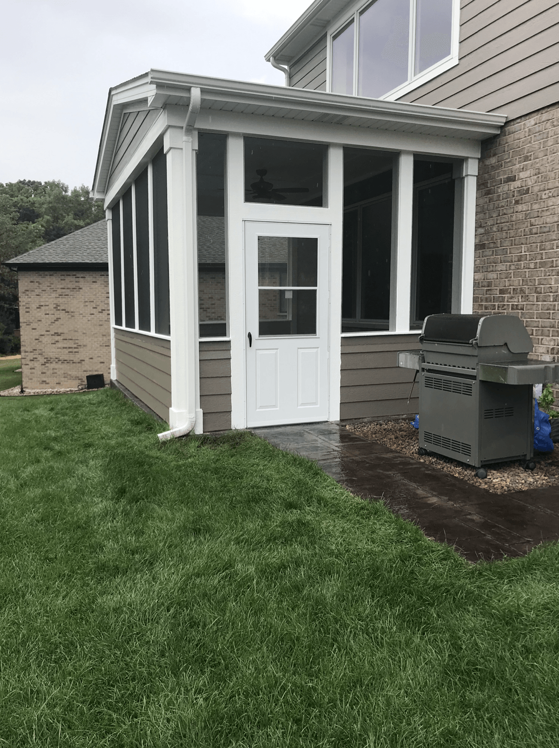 A screened in porch with a grill in the backyard of a house.