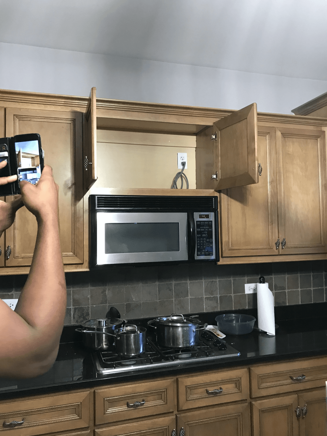 A person is taking a picture of a kitchen with a microwave.