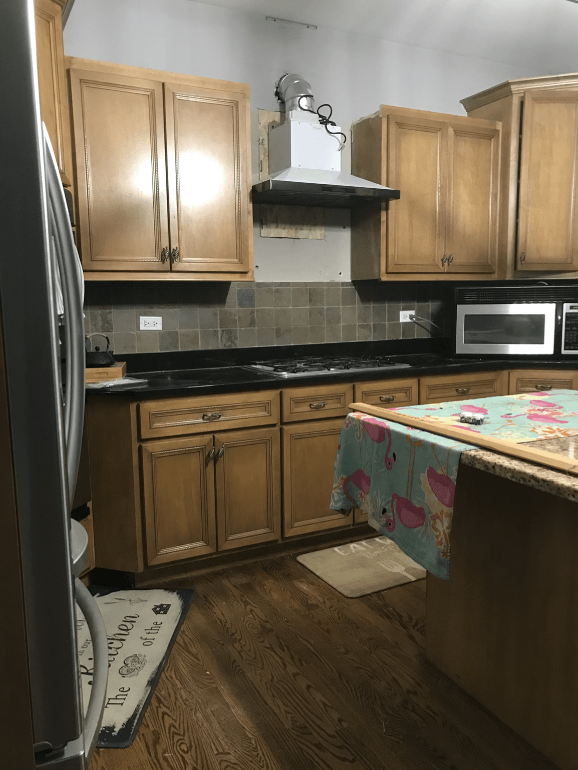 A kitchen with wooden cabinets , stainless steel appliances , a refrigerator and a microwave.