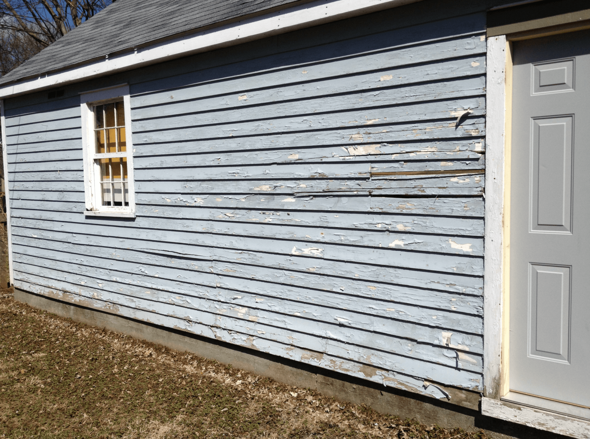 A blue house with peeling siding and a white door.