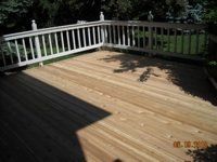 A wooden deck with a white railing and trees in the background.
