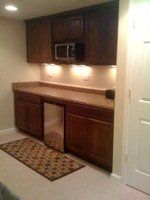 A kitchen with wooden cabinets , a microwave , a refrigerator and a rug.