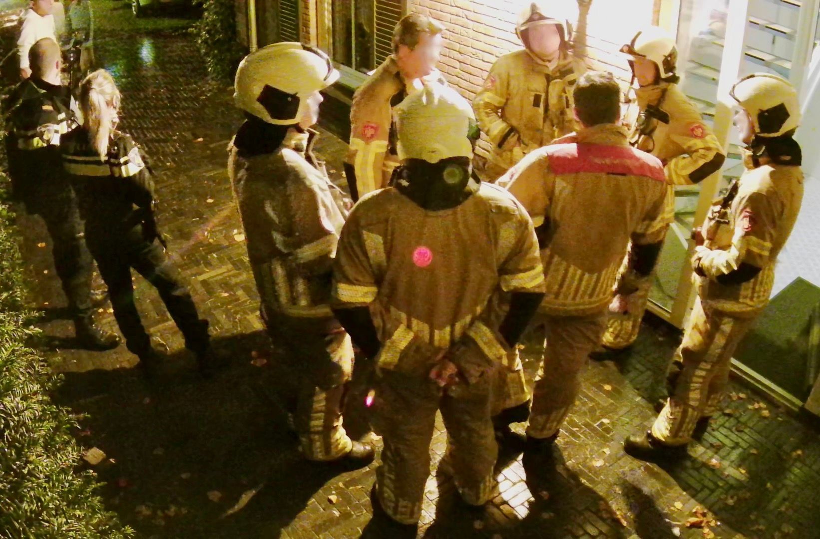 Een groep brandweerlieden staat 's nachts op de stoep.