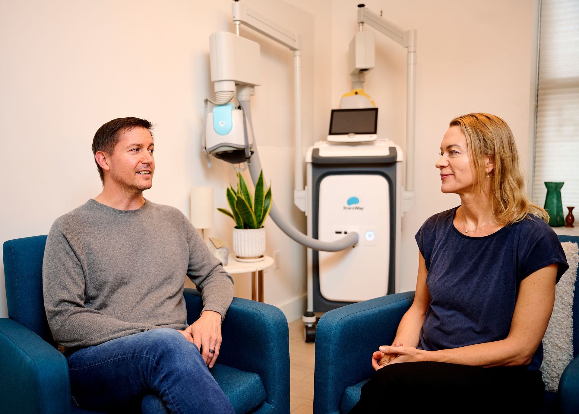 A man and a woman are sitting in chairs talking to each other in a room.