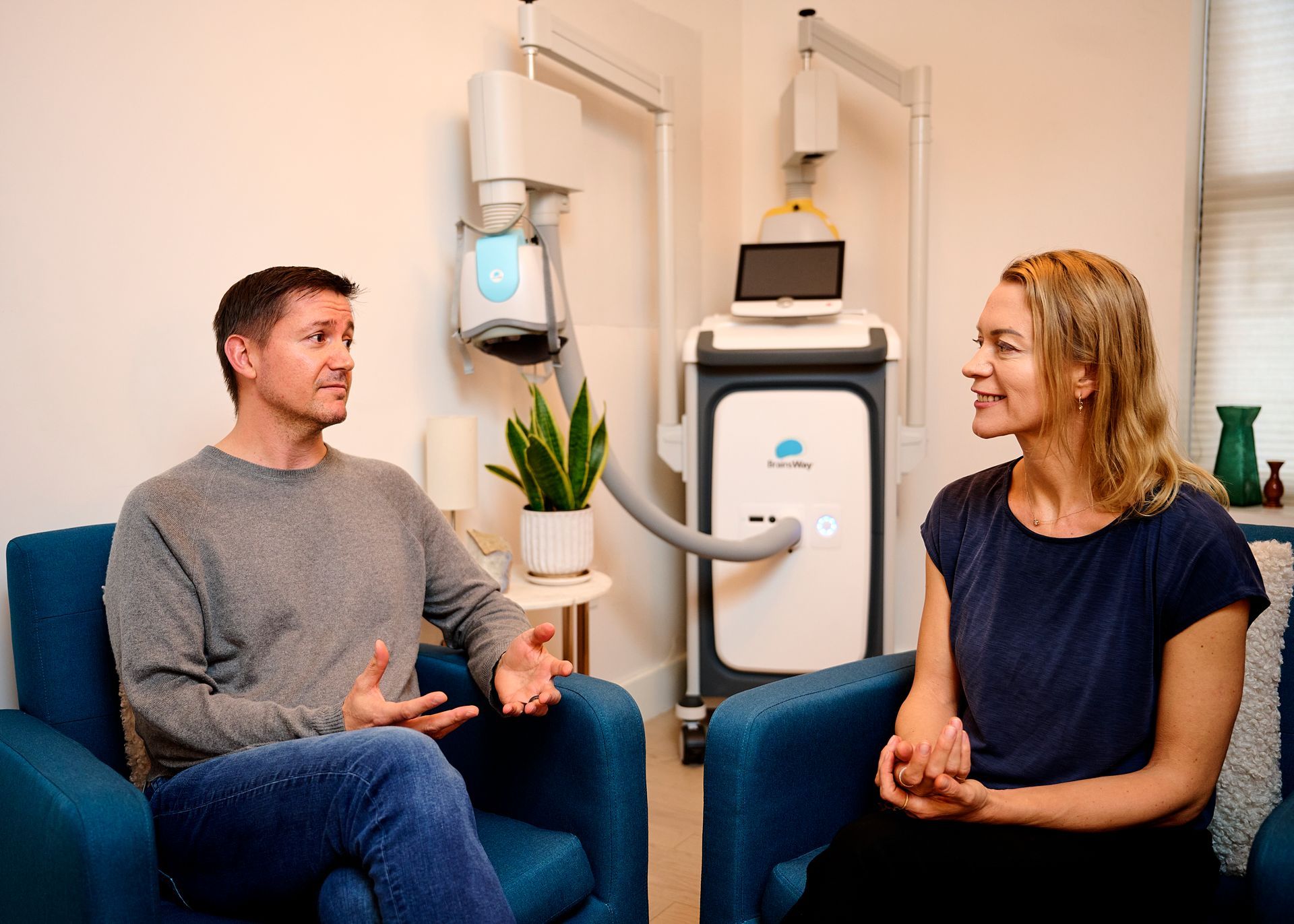 A man and a woman are sitting in chairs talking to each other in a room.