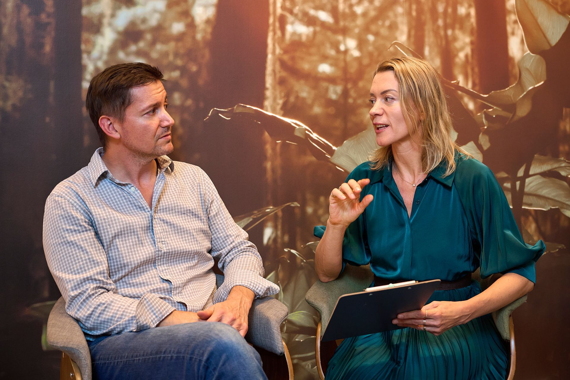 A man and a woman are sitting in chairs talking to each other.