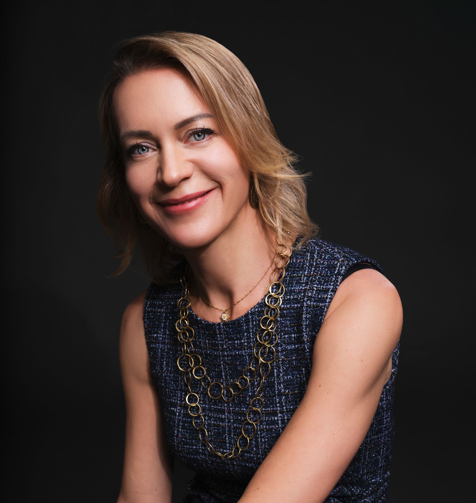 A woman wearing a blue dress and a gold necklace is smiling for the camera.
