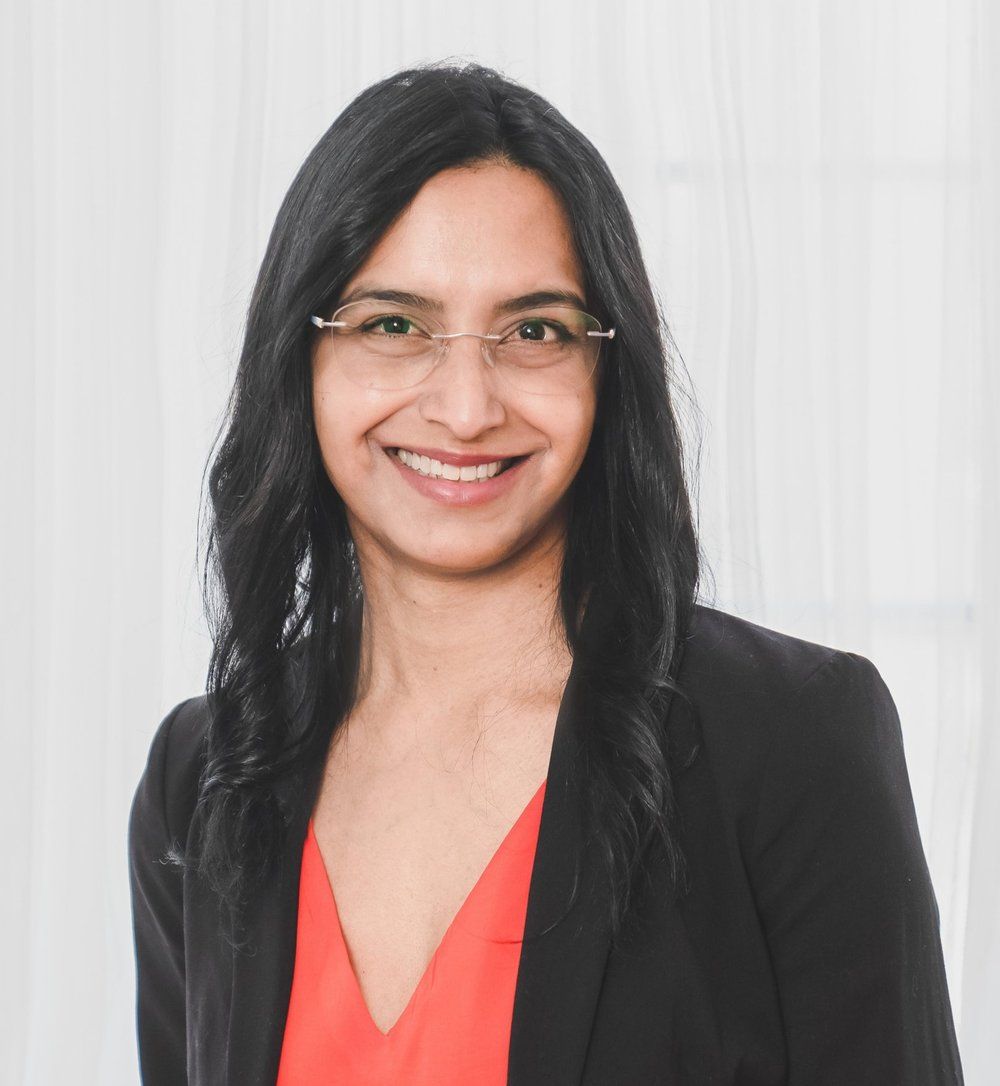 A woman wearing glasses and a black jacket is smiling for the camera.