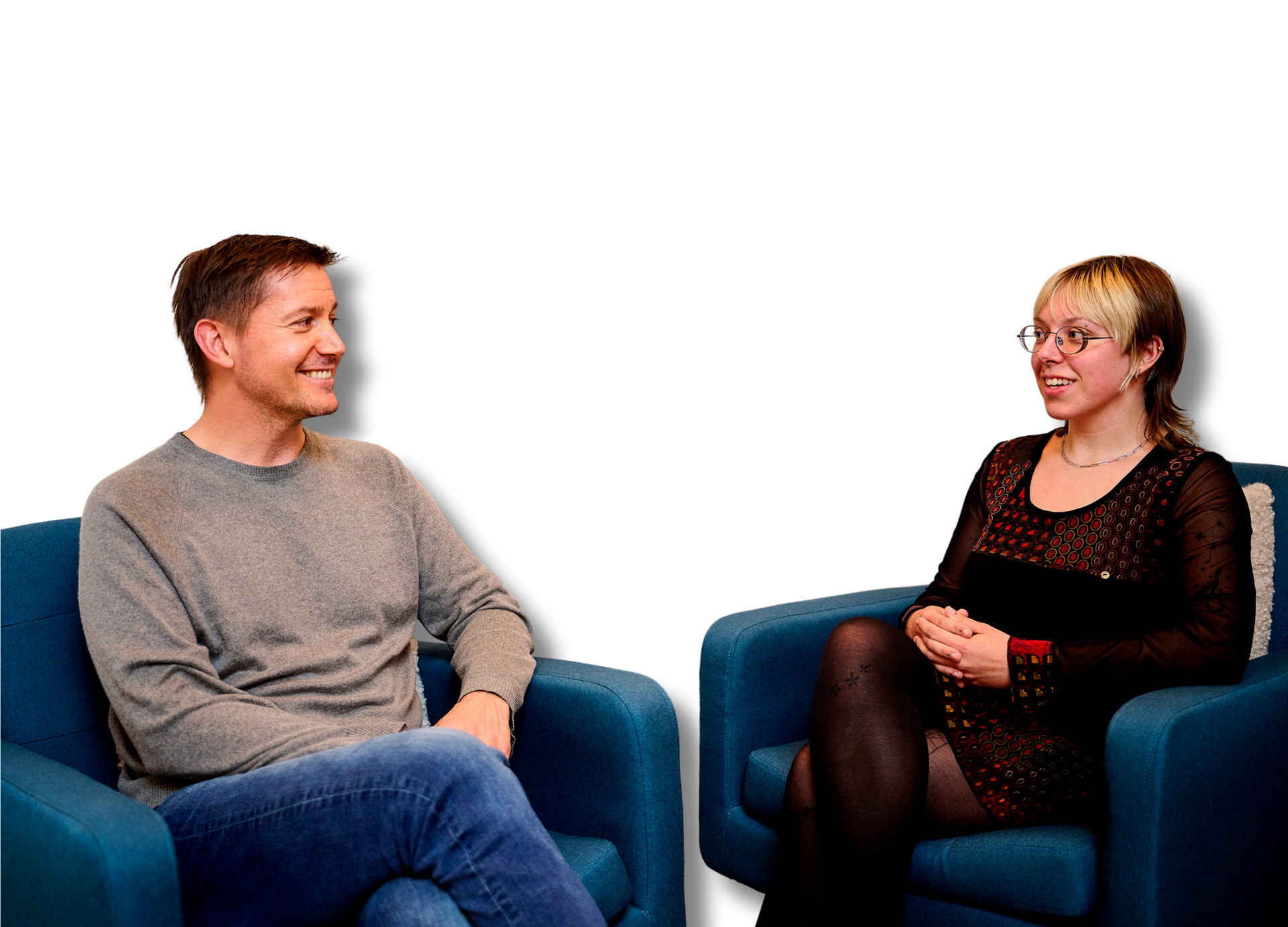 A man and a woman are sitting in blue chairs talking to each other.