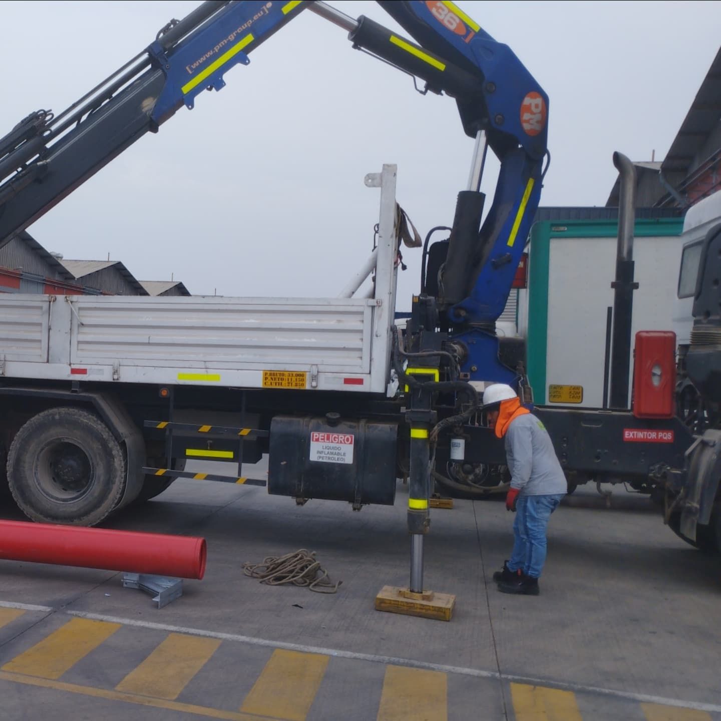 Un trabajador inspecciona una grúa montada en un camión con un tubo rojo largo, al aire libre.