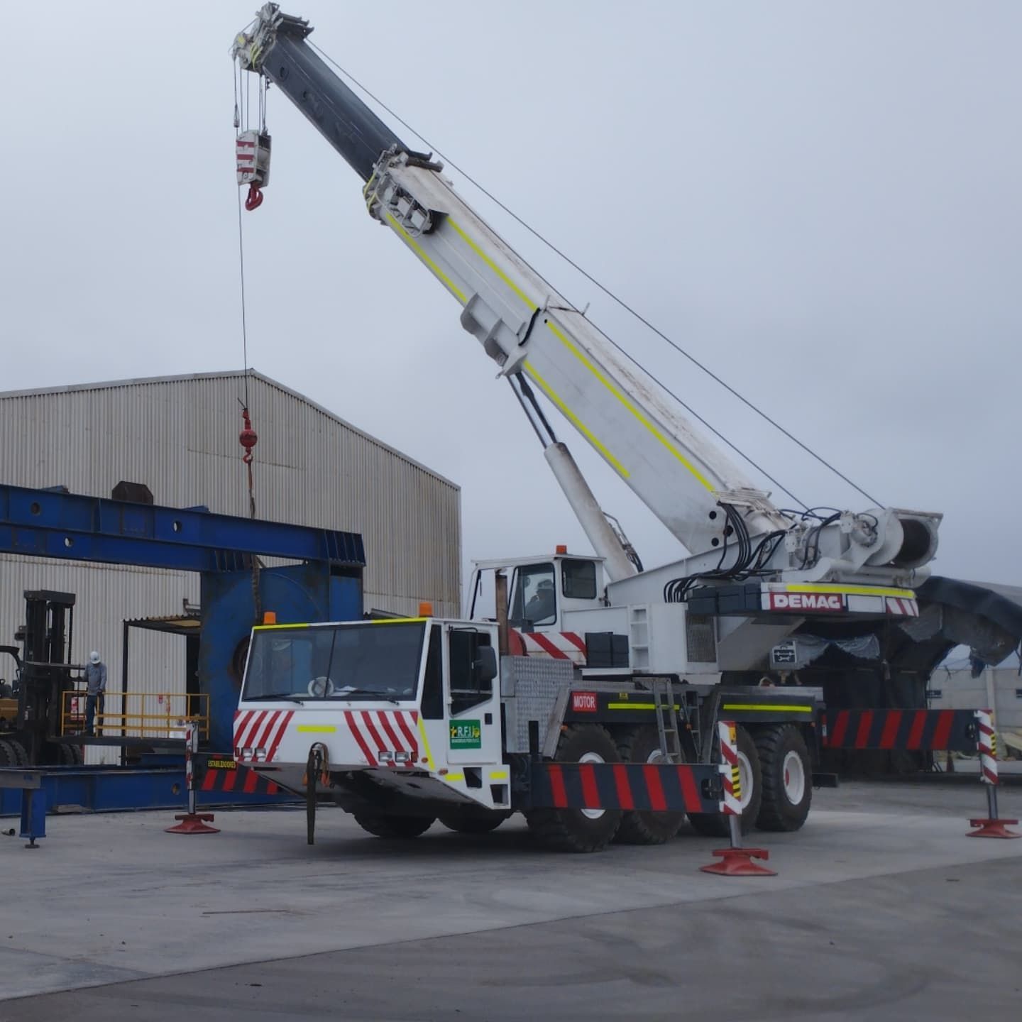 Una gran grúa blanca y roja levantando algo cerca de un edificio en un día nublado.