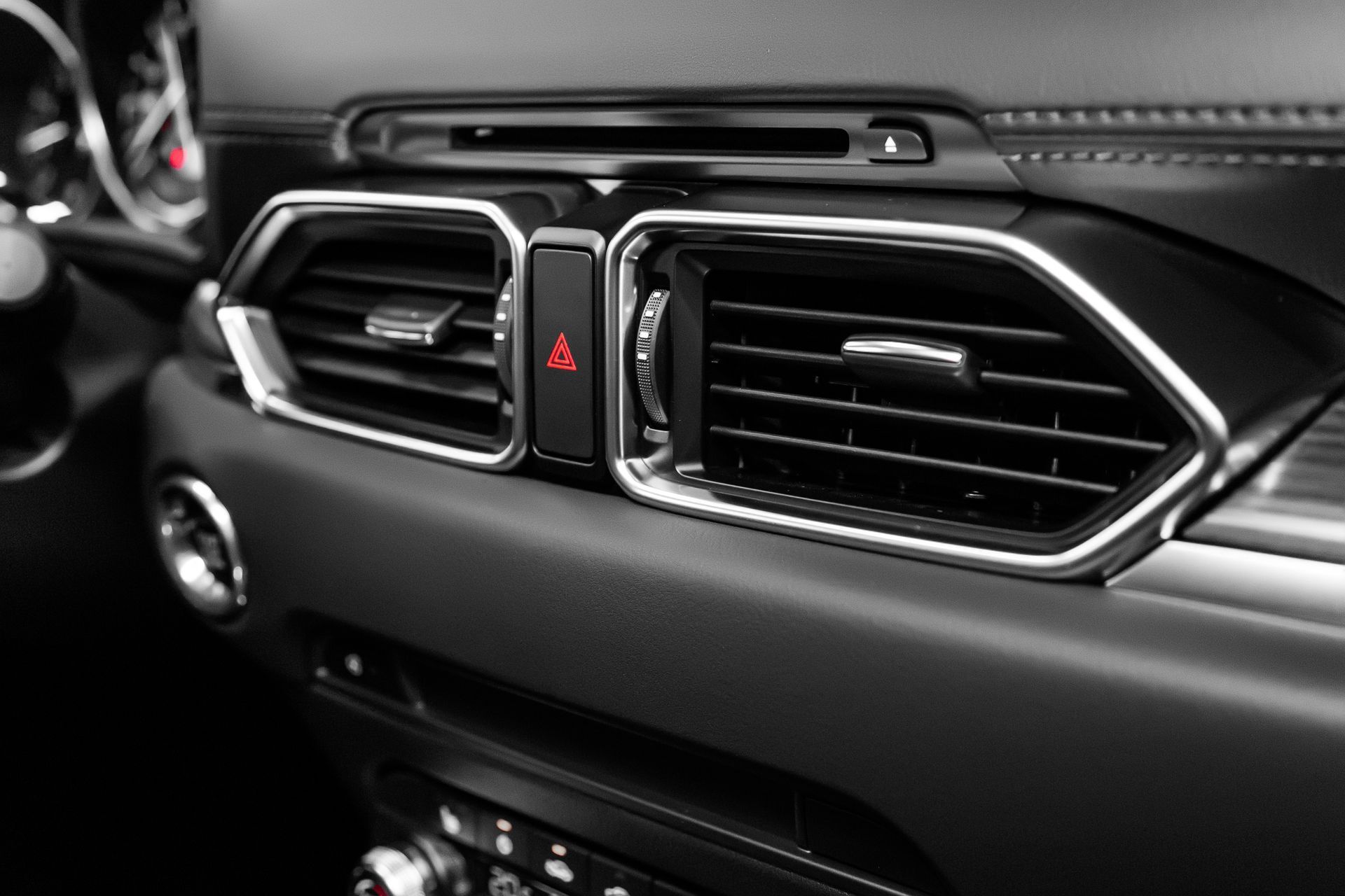 Car dashboard air vents and hazard light button in black and chrome trim