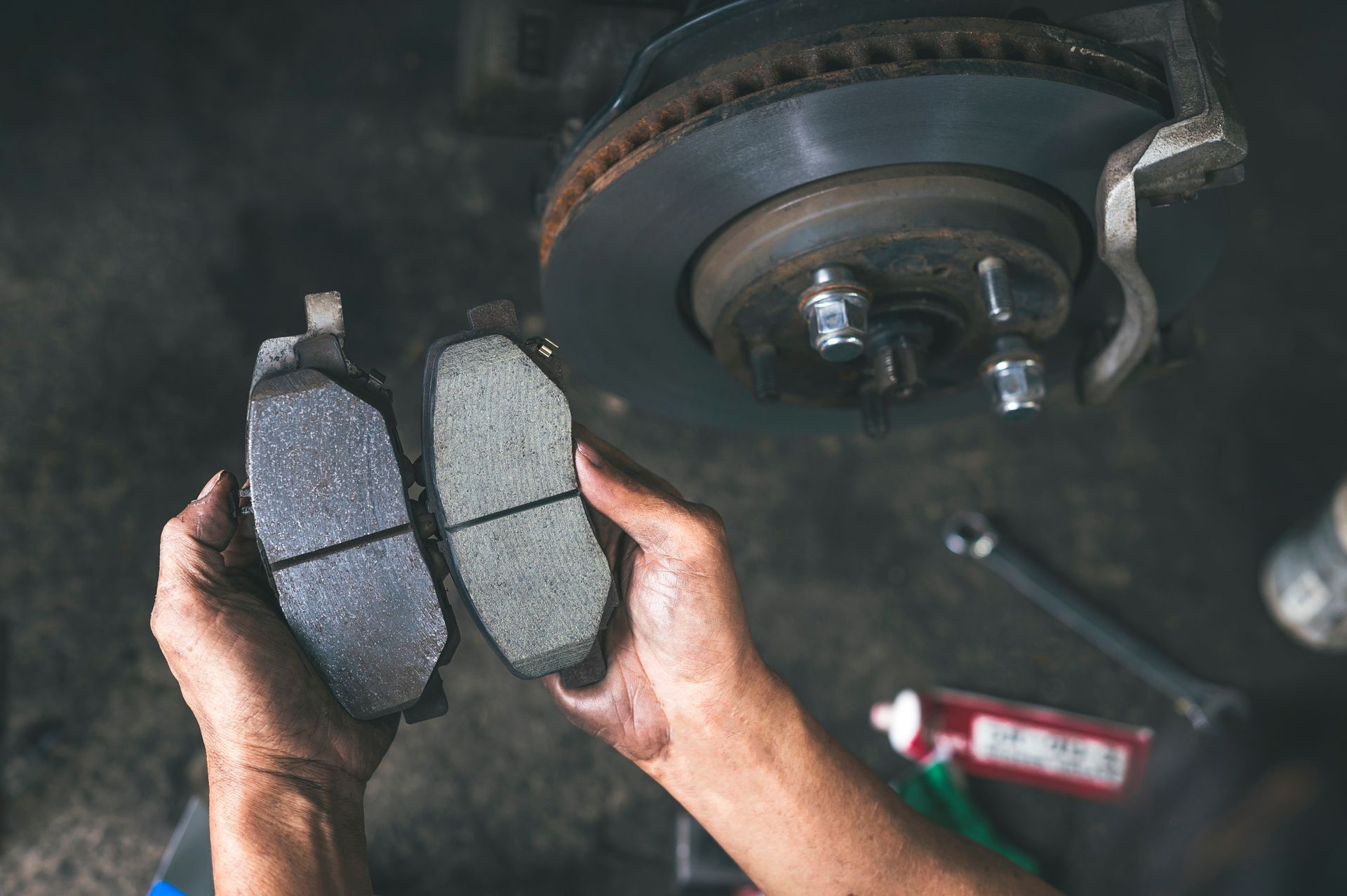 Hands holding two new brake pads beside a car wheel and rotor during repair