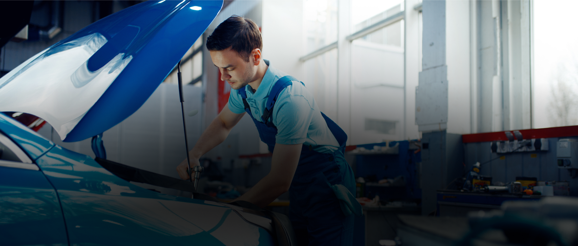 Mechanic working under open car hood in a bright auto repair shop