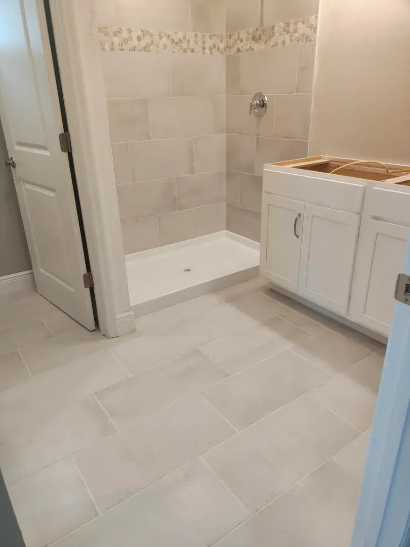 Bathroom with a white shower, vanity, and light-colored tile flooring.