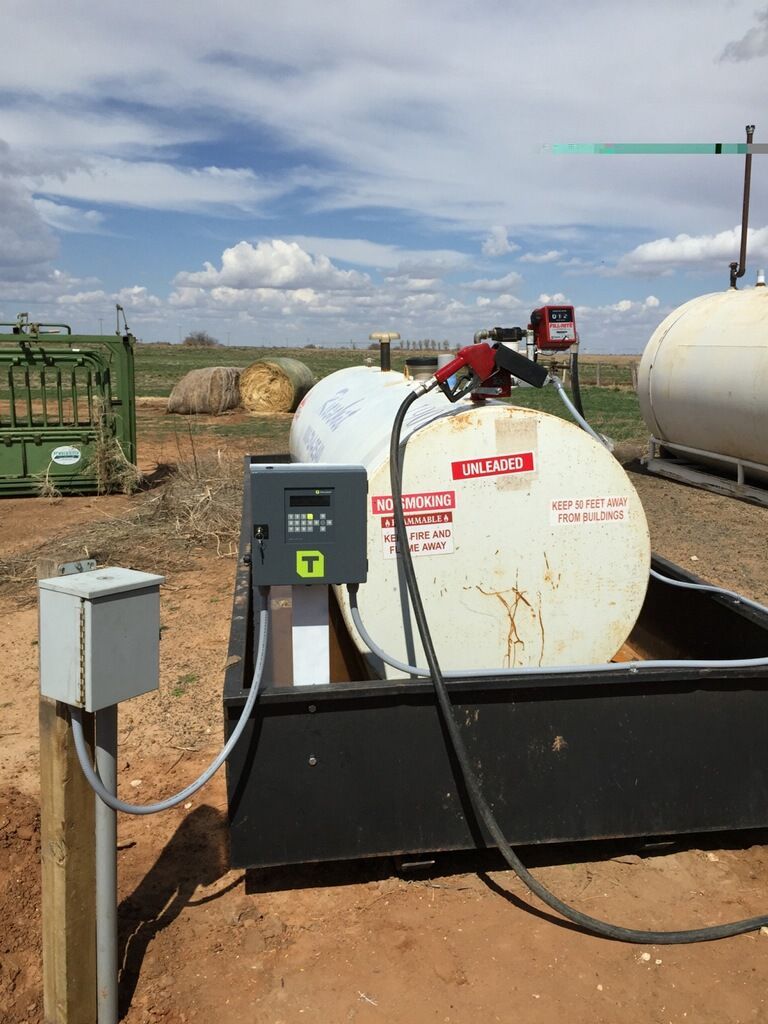 Fuel tank with pump in rural setting. Beige tank, black basin, blue sky.