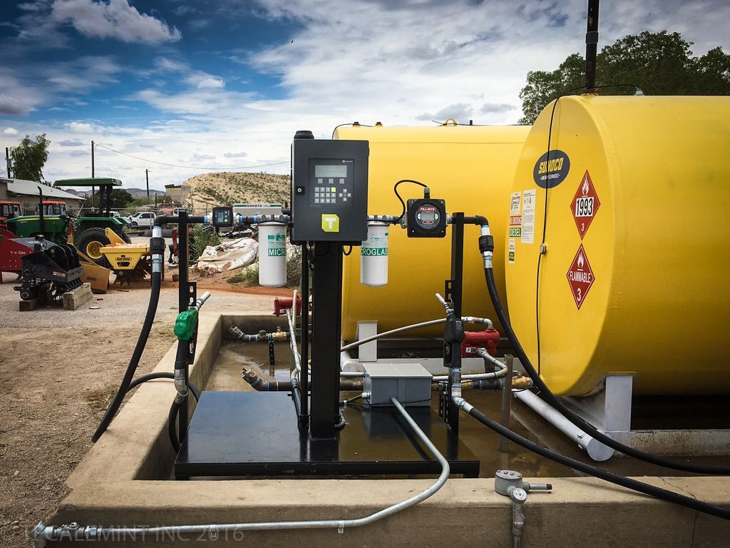 Fuel station with two yellow tanks, a black control panel, and dispensing nozzles. Outdoors, under a cloudy sky.