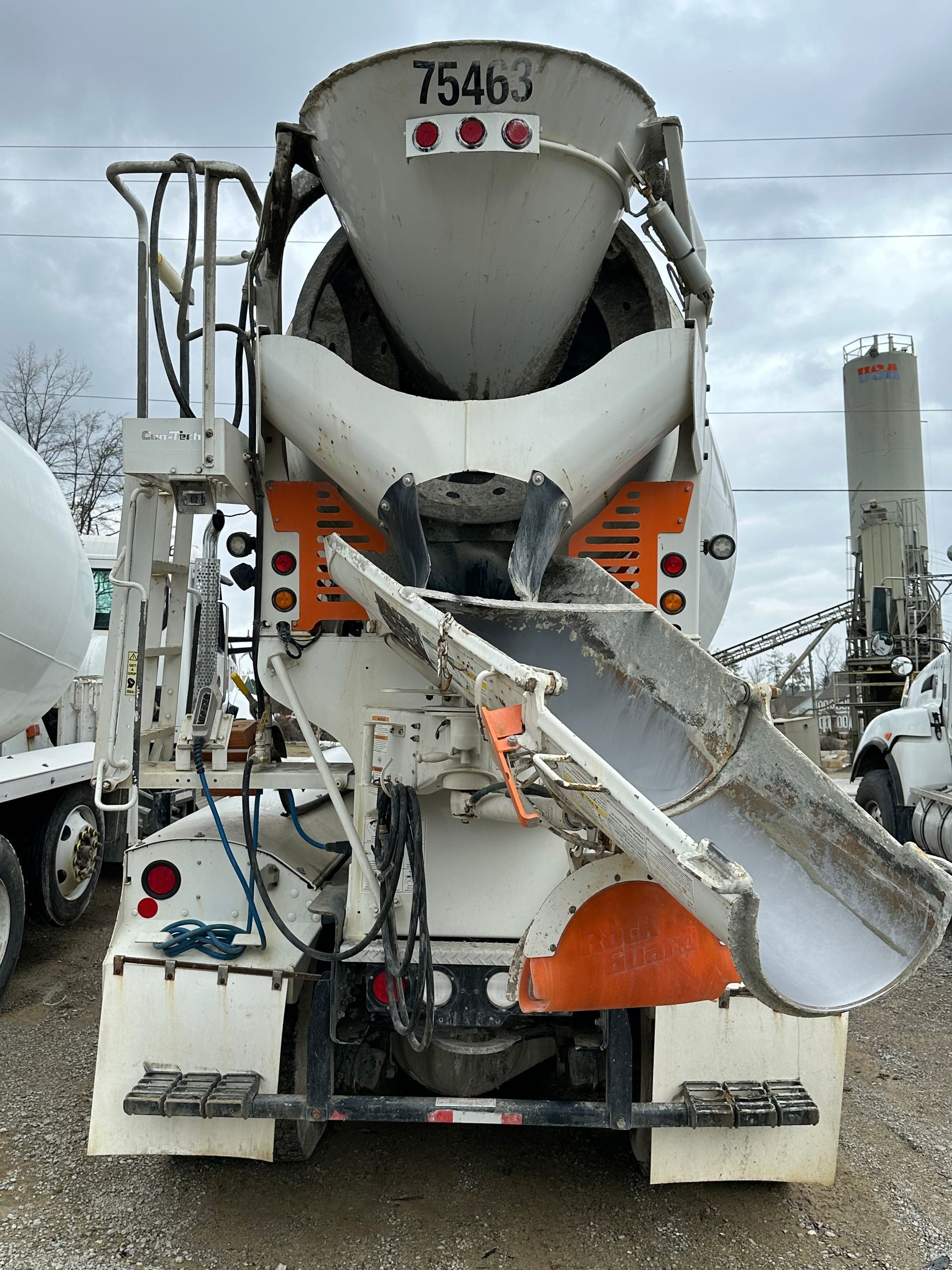 Concrete mixer truck, white and orange, discharging concrete.