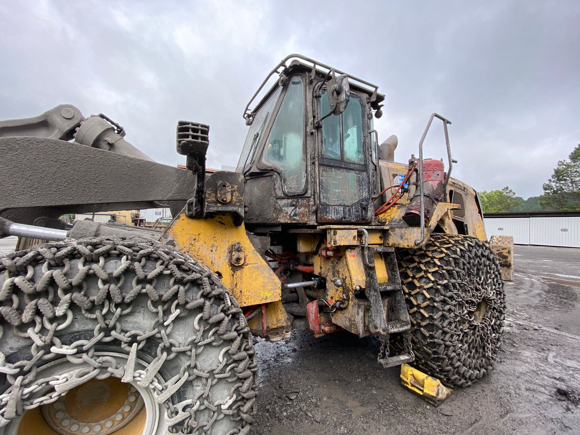 Yellow Caterpillar forestry machine covered in mud, with tire chains, parked outside.