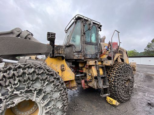 Yellow heavy machinery with chain-covered tires, covered in dirt, in an outdoor setting.