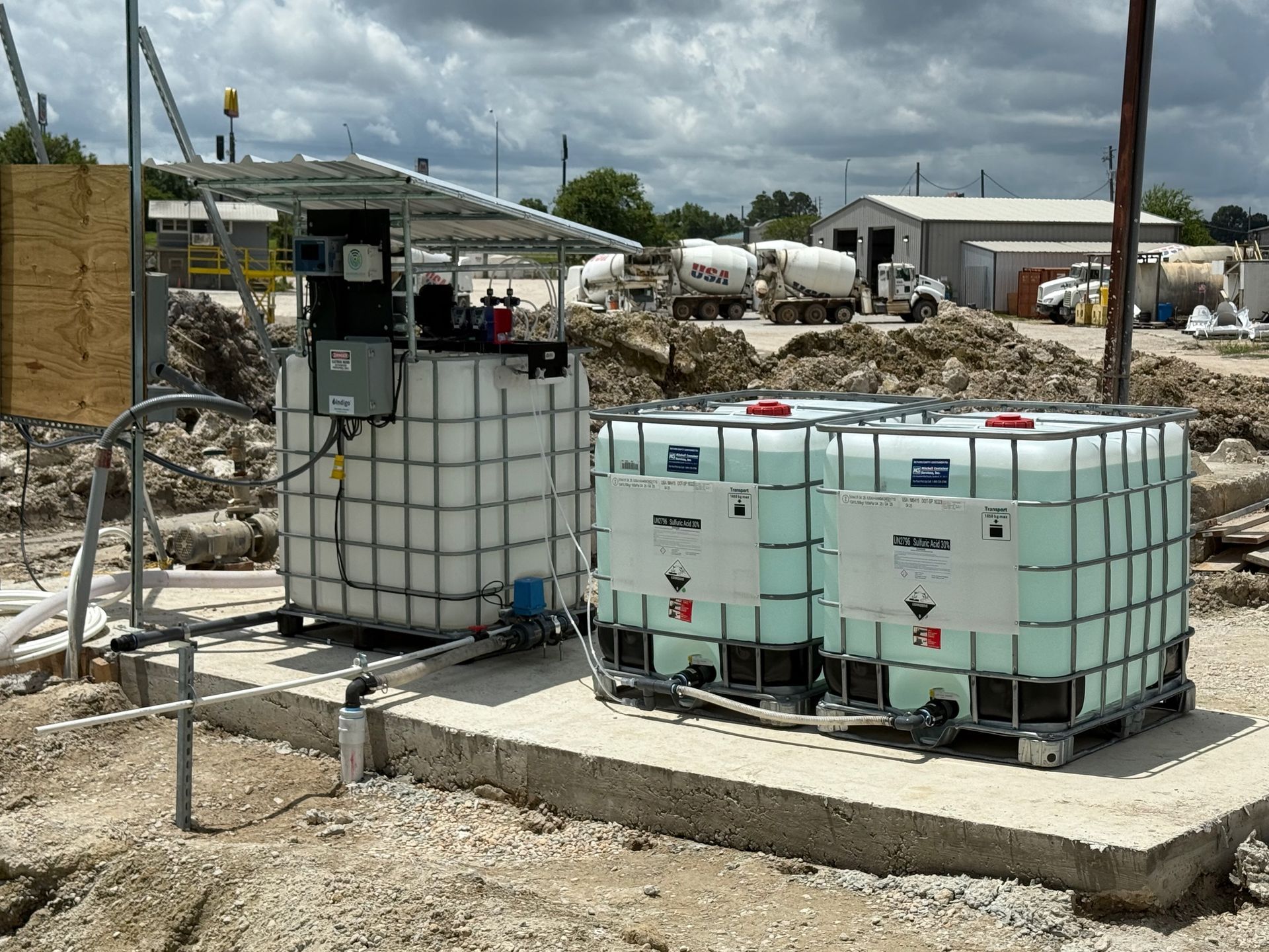 Industrial tanks on a concrete pad with equipment, construction site background.