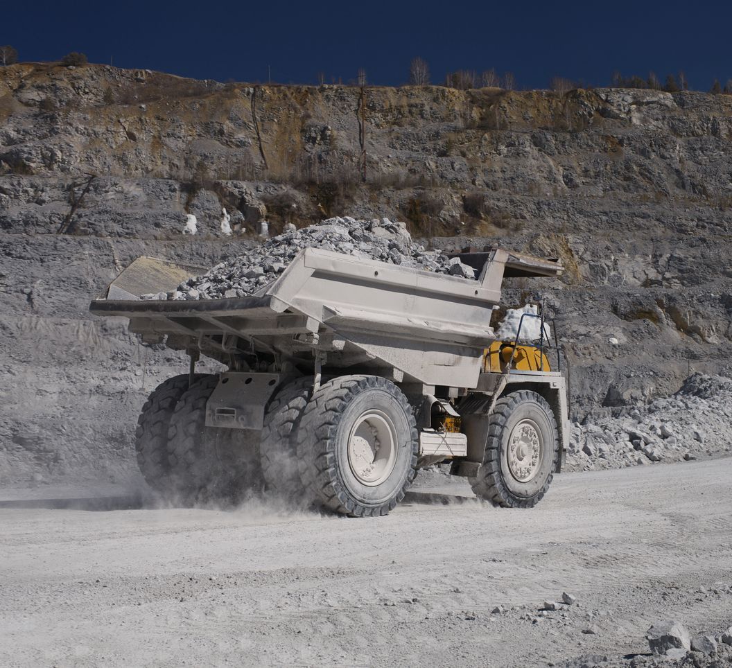 Dump truck carrying rocks in a quarry, dusty setting.