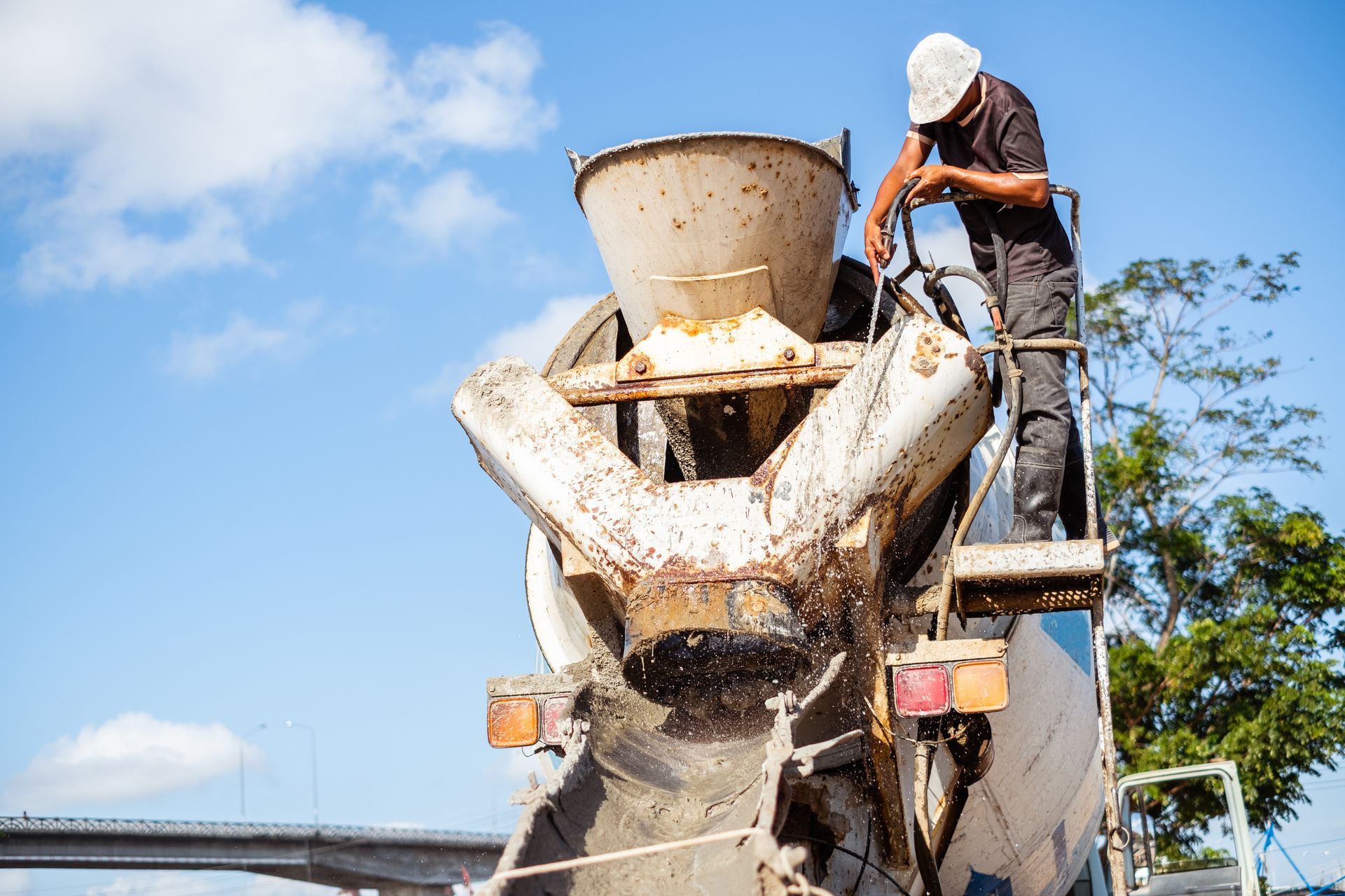 A worker operating a cement mixer on a construction site, pouring concrete. Bright blue sky background.