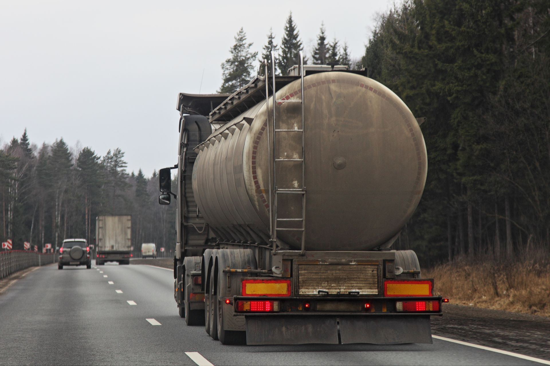Tanker truck on a highway, traveling away from the viewer; forest in the background.