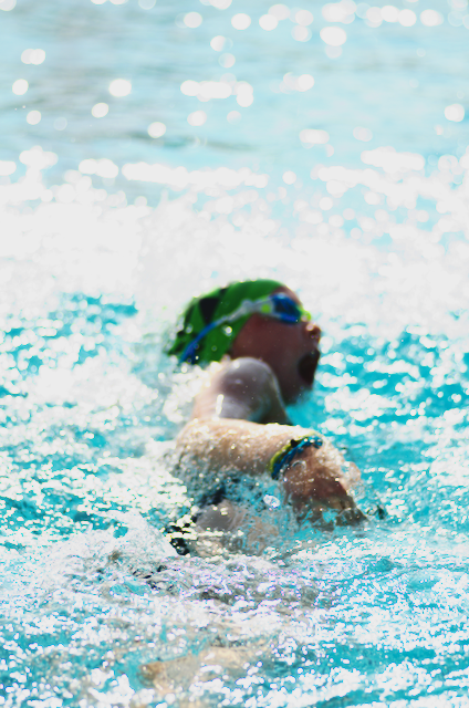 Swimmer in a green cap, goggles, and wristband, in a pool.