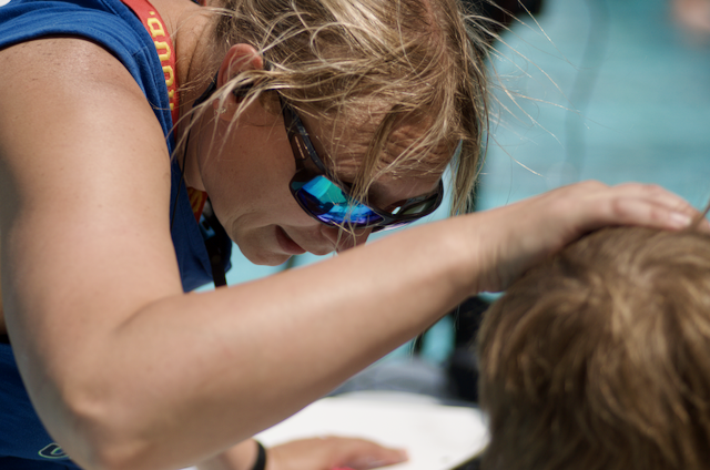 Woman adjusting goggles of child by a pool.