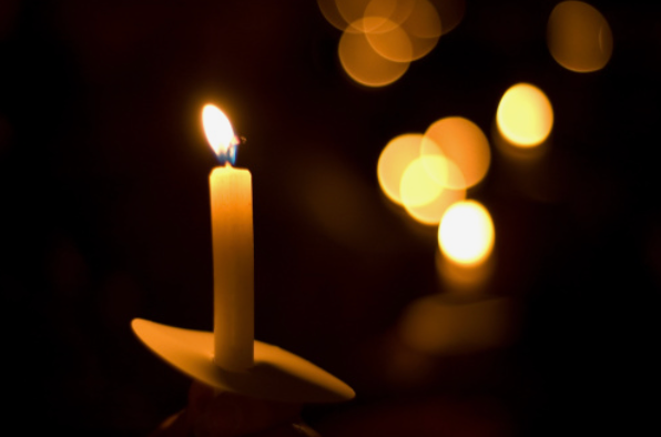 A Single candle glowing in the darkness. There are other candles glowing, out of focus.