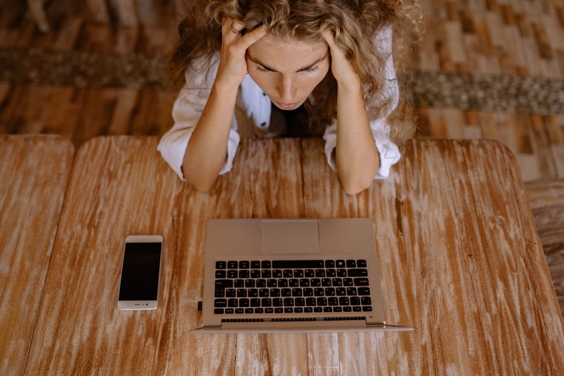 Woman sitting at her laptop and phone, appearing visibilty stressed and overwhelmed.