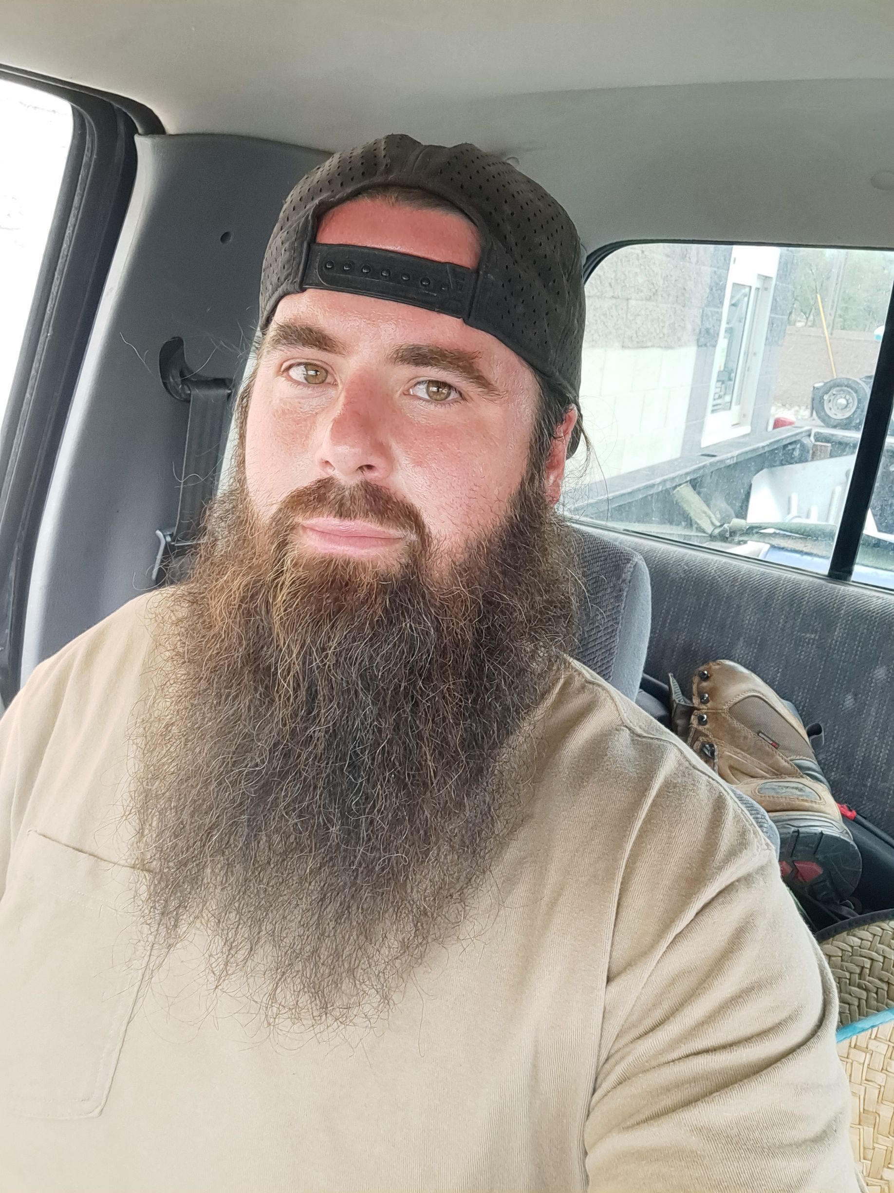 A man with a long beard is sitting in the back seat of a car.