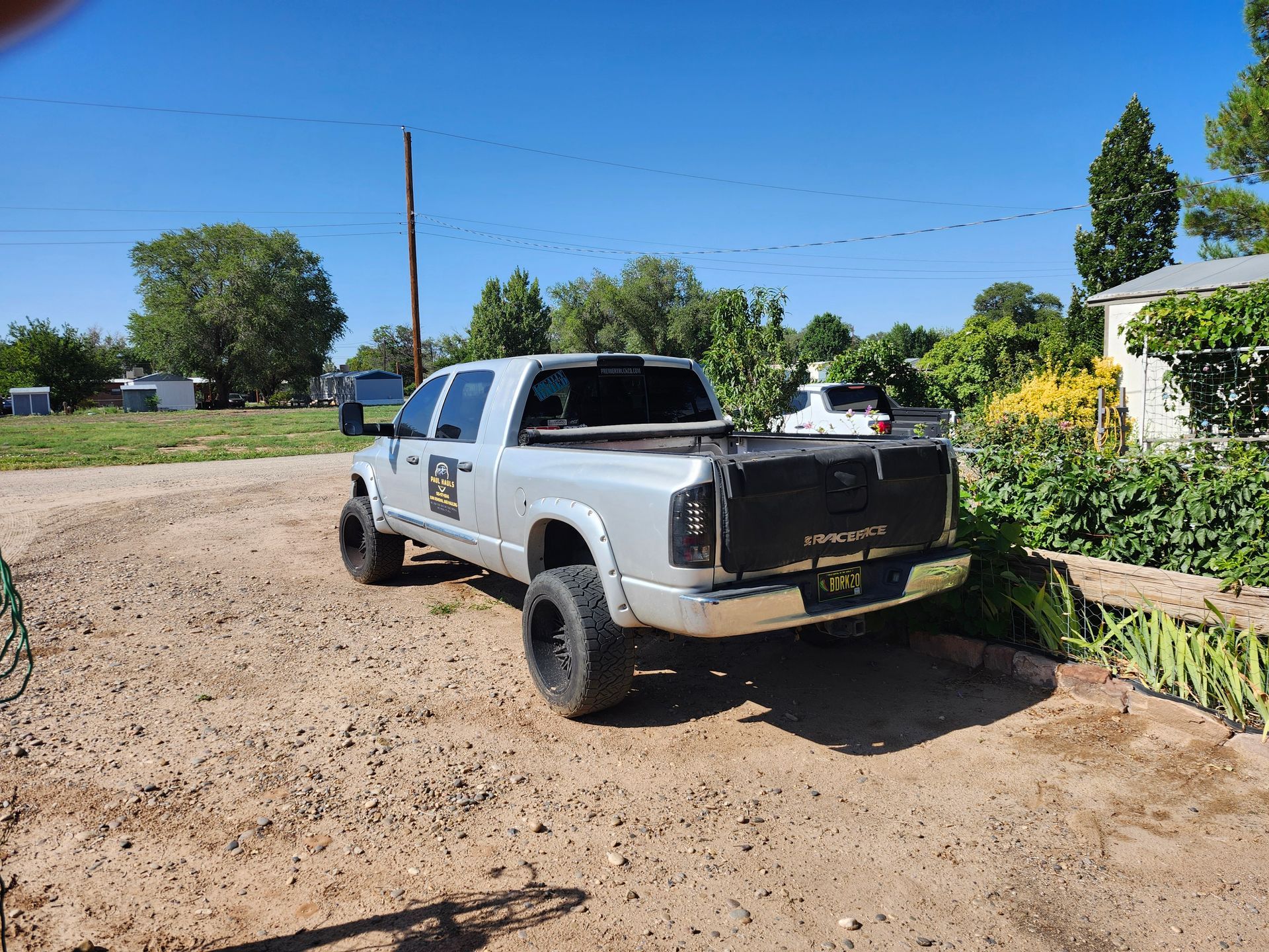 A white truck is parked in a dirt lot in front of a house.