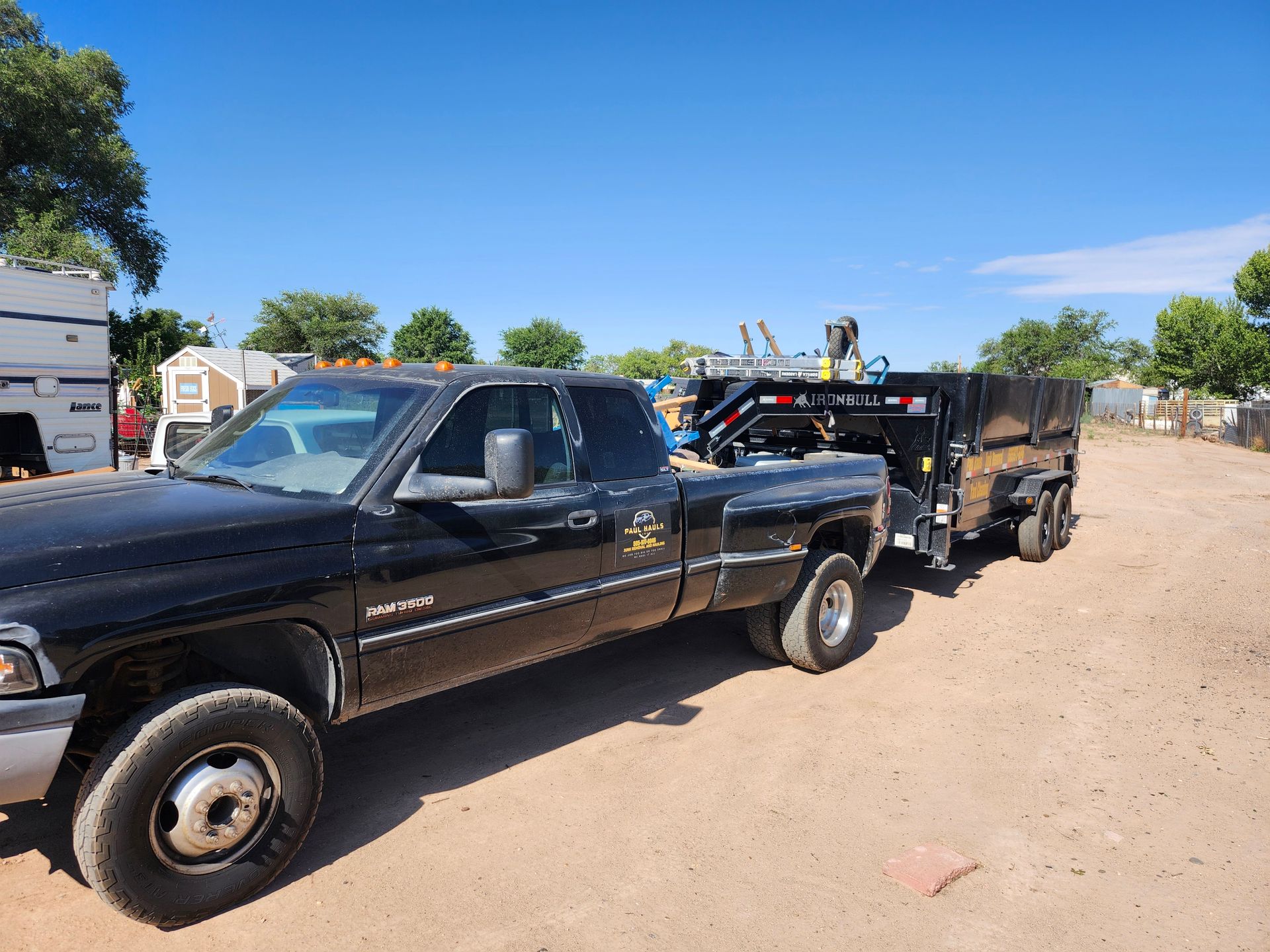 A black truck with a trailer attached to it is parked in a dirt lot.